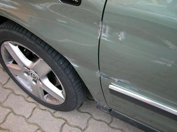 Schaden an der Seite eines silbergrünen Vans im Bereich der Vordertür
