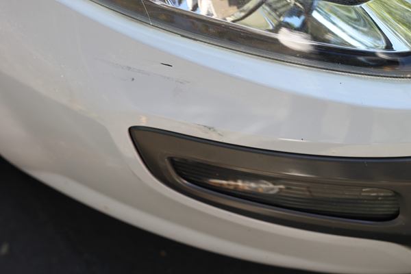 Detailaufnahme eines Schadens am Stoßfänger eines weißen Fahrzeugs