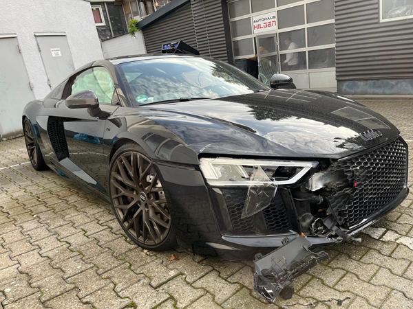 Schwarzer Sportwagen mit schwerem Frontschaden und ausgelösten Airbags vor einer Werkstatt